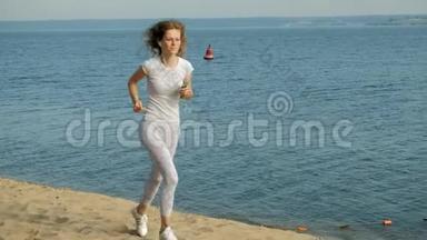 一个身材好的年轻女子在黎明时在海里从事体操。 她戴着耳机沿着海岸跑