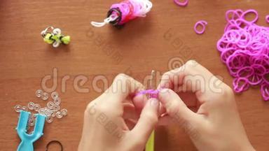 小女孩编织橡皮筋的腕带。 编织的彩色橡皮筋