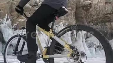 人正骑自行车在冰窟附近。 有冰洞和冰柱的岩石非常美丽。 骑自行车的人穿着