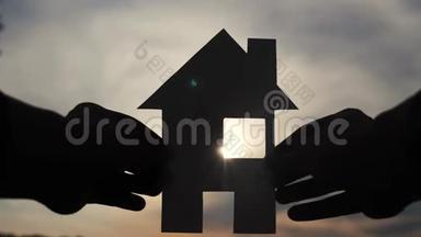幸福家园建设理念.. 在日落的剪影阳光下，一个人手里拿着一个纸房子。 生活