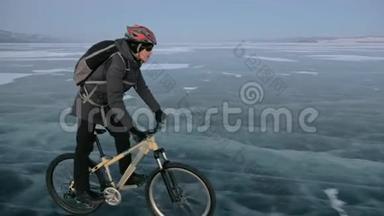 人在冰上骑自行车。 骑自行车的人穿着灰色的羽绒服，背包和头盔。 冰冻的冰