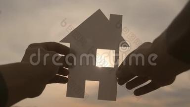 幸福家园建设理念.. 他手里拿着一个纸生活方式的房子，手里拿着夕阳的剪影