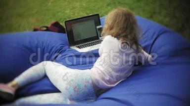 年轻女子用手提电脑，躺在公园的一个休息区，软泡芙上