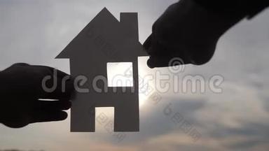 幸福家园建设理念.. 在日落的剪影阳光下，一个人手里拿着一个纸房子。 生态