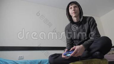 青少年和操纵杆男子头罩毛衣吸收在线电子游戏。 少年在兜帽里玩电子游戏