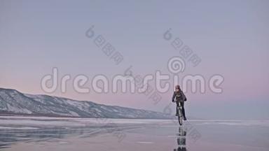 人在冰上骑自行车。 骑自行车的人穿着灰色的<strong>羽绒服</strong>，背包和头盔。 冰冻的冰