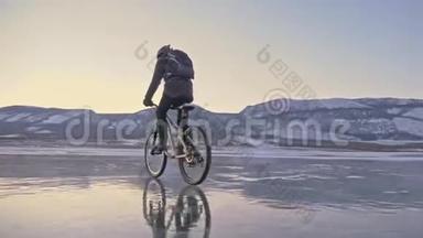 人在冰上骑自行车。 骑自行车的人穿着灰色的<strong>羽绒服</strong>，背包和头盔。 冰冻的冰