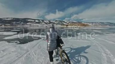 女人在冰上骑着自行车走着。 女孩穿着银色的羽绒服，背包和头盔。 冰冰