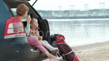 美丽的年轻女子和她的小女儿正坐在一条海边的一辆敞篷汽<strong>车</strong>的<strong>后备箱</strong>里