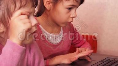 孩子们在笔记本电脑里玩。 两个<strong>小</strong>女孩印在笔记本电脑上。 两个<strong>姐姐</strong>坐在橙色的沙发上看着一圈
