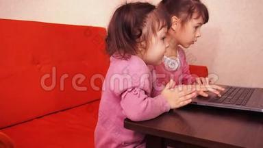 孩子们在笔记本电脑里玩。 两个<strong>小</strong>女孩印在笔记本电脑上。 两个<strong>姐姐</strong>坐在橙色的沙发上看着一圈