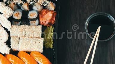 时尚的寿司放在黑色的木制背景上，旁边是酱油和中国竹签。 各种寿司卷