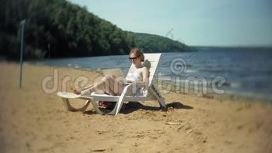 一个穿着白色比基尼的年轻女孩躺在<strong>沙滩上</strong>的躺椅<strong>上晒太阳</strong>，正在使用笔记本电脑