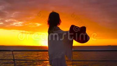 美丽的日落时分，穿着白色连衣裙和戴着帽子的年轻迷人女子在海上背景下摆姿势