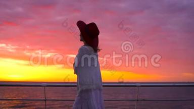 美丽的日落时分，穿着白色连衣裙和戴着帽子的年轻迷人女子在海上背景下摆姿势