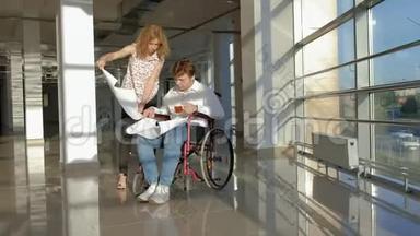 一位坐在轮椅上的残疾商人在窗户上，一张大纸上写着一张照片，与一位同事讨论工作