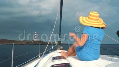 戴着黄色帽子的女人和穿着蓝色衣服的女孩在海洋的夏季在游艇上休息