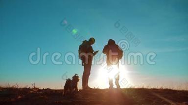 团队合作。 两名游客徒步旅行，男人和狗带着背包在日落时去徒步旅行。 慢动作录像。 旅行和徒步旅行者