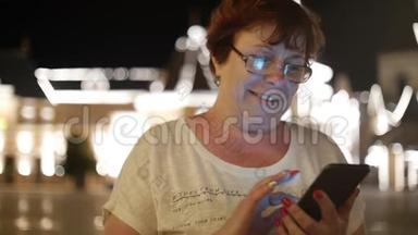 在一个夜晚的城市里，女人用手机穿过街道，在背景的夜晚城市里