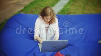 年轻女子用手提电脑，躺在公园的一个<strong>休息区</strong>，软泡芙上