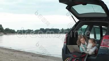 美丽的年轻女子和她的小女儿正坐在海边的一辆敞篷汽<strong>车</strong>的<strong>后备箱</strong>里