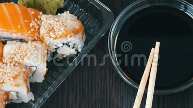 时尚的寿司放在黑色的木制背景上，旁边是酱油和中国竹签。 各种寿司卷