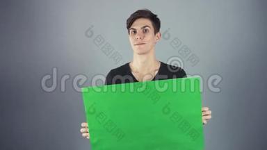 微笑穿着黑色衬衫的年轻人拿着绿色钥匙片海报，灰色背景