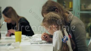 <strong>孩子</strong>们女孩坐在教室的桌子旁，用手指和油漆<strong>画画</strong>。 带着他们