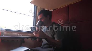 男人坐在<strong>火车车厢</strong>上，手里拿着智能手机，生活方式是喝咖啡和茶。 慢动作