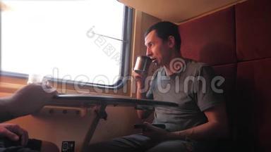 男人坐在火车车厢上，手里拿着智能手机铁路，喝着咖啡和茶。 慢动作视频。 男人
