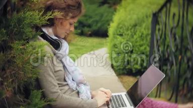 有笔记本电脑的女人在一个美丽的绿色公园的长凳上放松。 一个常年在<strong>树洞</strong>里工作的年轻女人