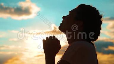 女孩在祈祷。 女孩双手交叉祈祷剪影日落。 慢动作视频。 女孩双手叠起她的生活方式