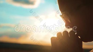 女孩在祈祷。女孩双手合十，祈祷夕阳的剪影。慢动作视频。女孩双手合十祈祷