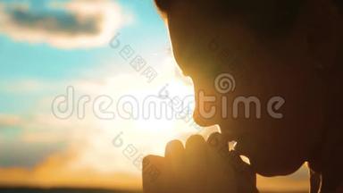 女孩在祈祷。 女孩在日落时交叉双手祈祷剪影。 慢动作视频。 女孩双手交叉祈祷