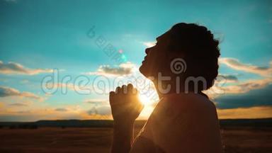 女孩在祈祷。 女孩在日落时<strong>交叉双手</strong>祈祷剪影。 慢动作视频。 女孩<strong>双手</strong>合拢