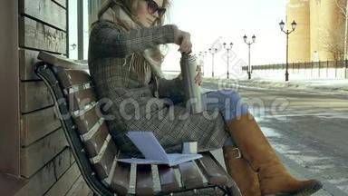 坐在长凳上的一个春天公园里，一个年轻的女人从一个热水瓶里喝茶
