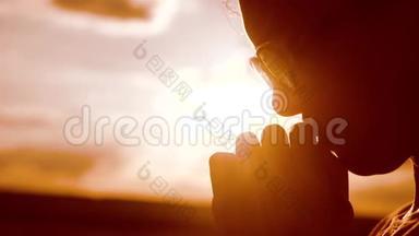 女孩祈祷。 女孩在日落时双手交叉祈祷剪影。 慢动作视频。 女孩双手交叉祈祷