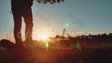 人类游客正坐在篝火旁聚会，在大自然野营的剪影下晒日落。度假男士剪影