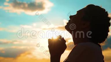 女孩在祈祷。 女孩在日落时交叉双手祈祷剪影。 慢动作生活方式视频。 女孩双手合拢