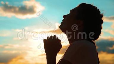 女孩在祈祷。 女孩在日落时双手交叉祈祷剪影。 慢动作视频。 女孩的生活方式