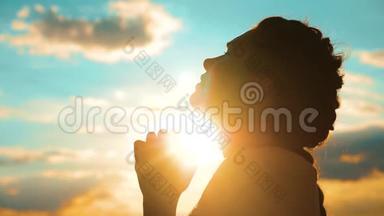 女孩在祈祷。 女孩在日落时交叉双手祈祷剪影。 慢动作视频。 女孩双手合拢