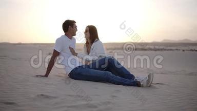 年轻的男人和女人坐在沙漠中，美丽的夫妇，女孩和男人沙丘景观背景。 <strong>轻微</strong>的黄昏。 浪漫浪漫