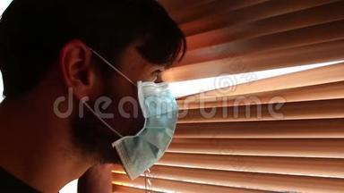 一个年轻的帅哥戴着医用口罩透过百叶窗看着。