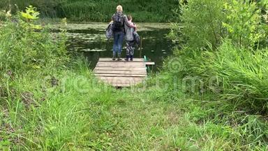 母亲和儿子带着背包的游客，徒步旅行者沿着长满青草的小路走到河边，欣赏大自然
