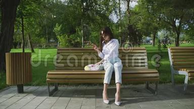 在夏天的公园里，年轻的女人坐在长凳上，手里拿着装满水果和蔬菜的棉网购物袋。 零废物