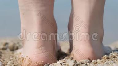 一个人的特写`他的脚在海滩上，走进水里。 背面