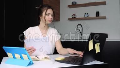 检疫期间厨房里的年轻女子。 女孩坐在桌子旁，手里拿着<strong>文件</strong>，在笔记本电脑<strong>键盘</strong>上打字。 工作