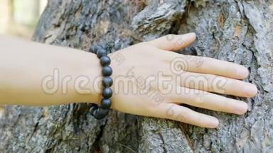 一个女人的手拿着一个手镯`特写，手镯正小心翼翼地抚摸着树