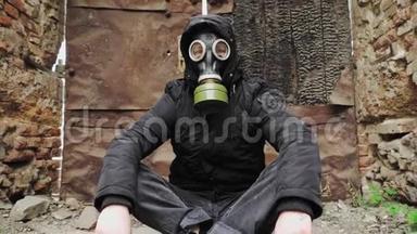 戴着防毒面具和黑色帽衫的人坐在一座被毁的废弃建筑的背景上。 后世界<strong>末日</strong>。