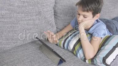 男孩躺在沙发上，家里有数字平板电脑。 技术、<strong>远程教育</strong>、在线学习、玩游戏